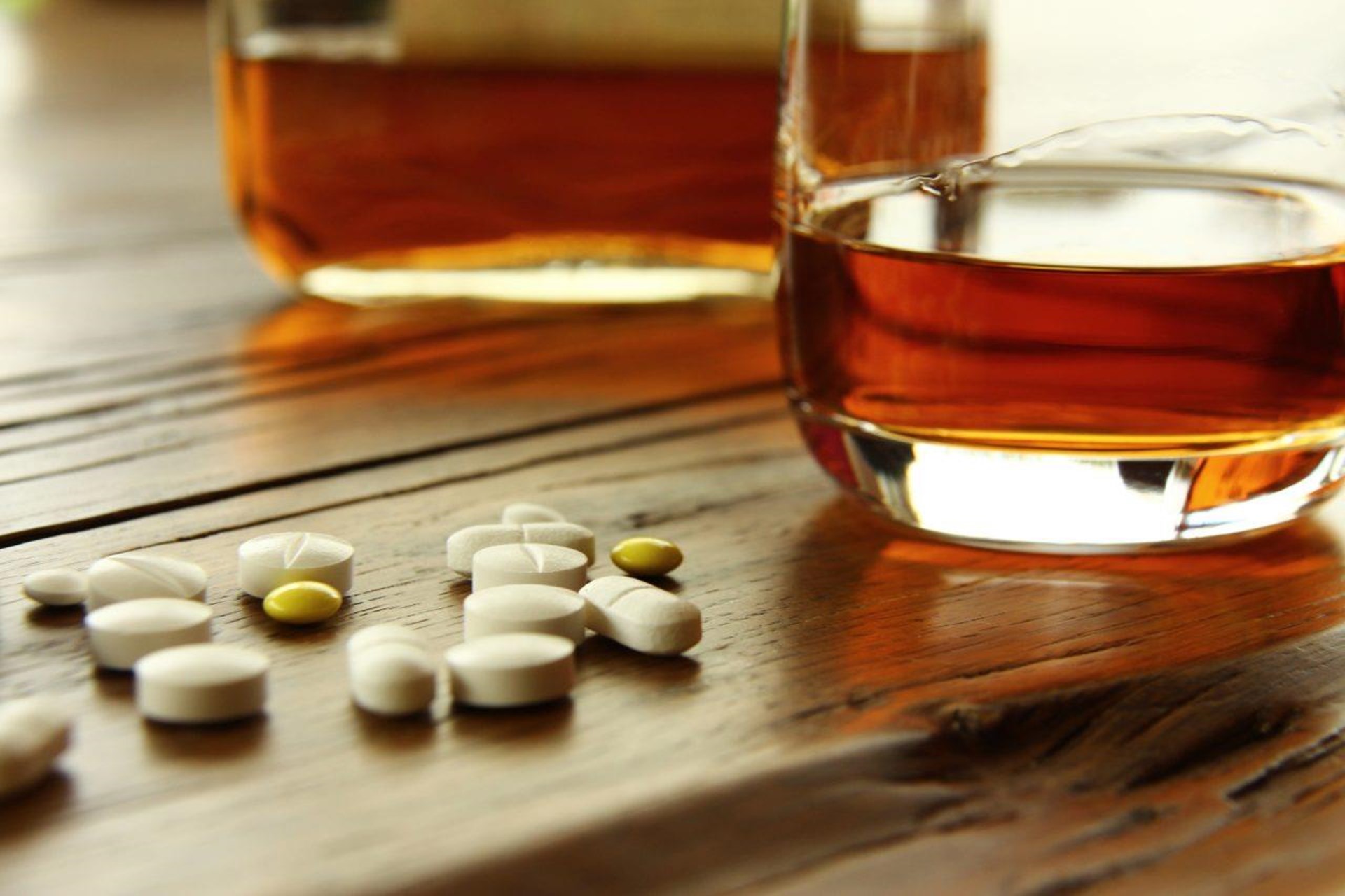 Tabeletten liegen neben einem Glas Whiskey auf einem Tisch.