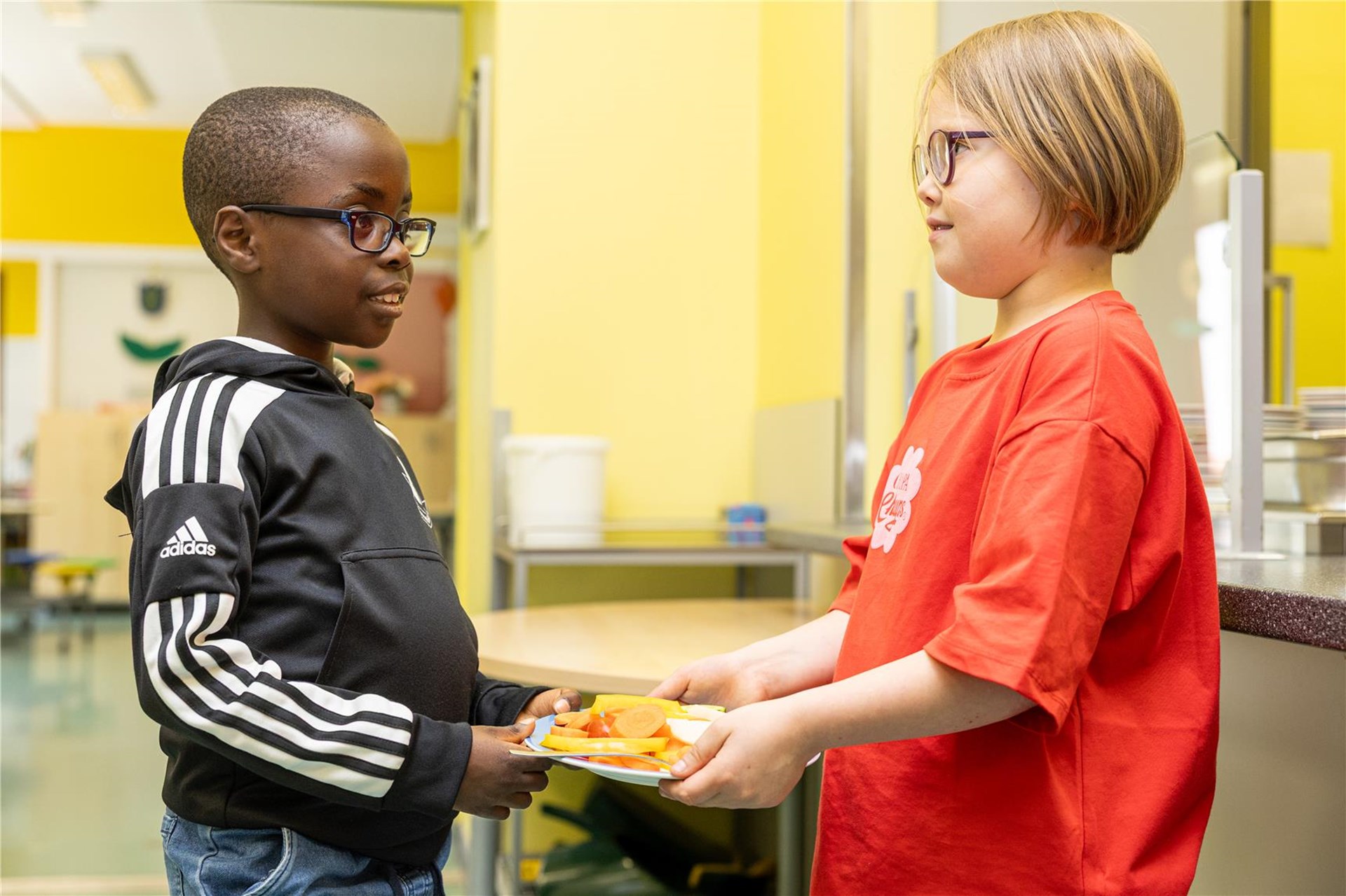 Ein Junge reicht dem anderen Jungen ein Teller mit essen.
