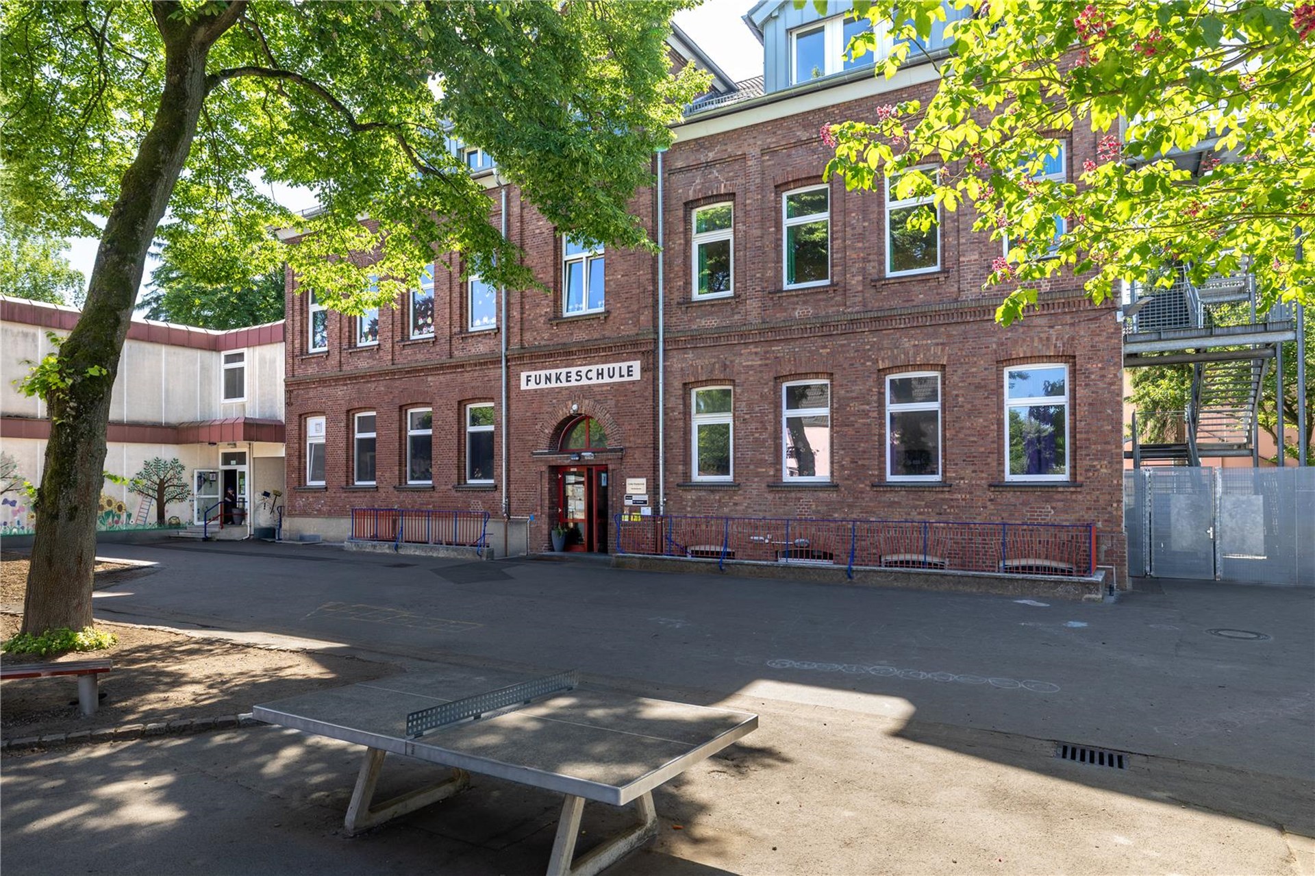 Nahaufnahme eines Backsteingebäudes, davor ein Schulhof