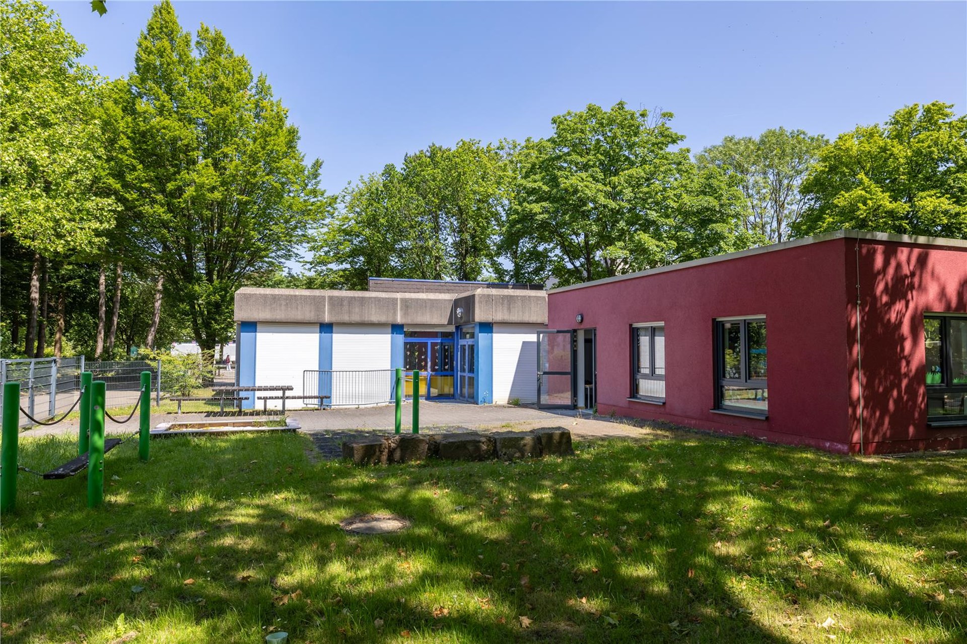 Ein rotes eingeschossiges Gebäude mit Flachdach, davor eine Wiese