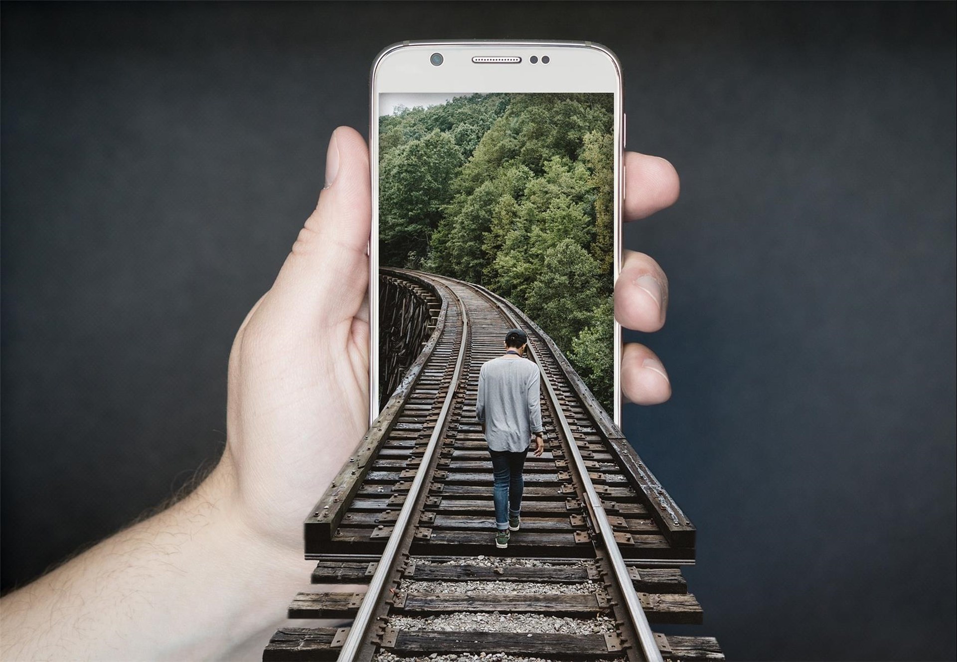 Fotocollage: Ein Mann geht über Eisenbahnschienen, die in einem Handy enden.