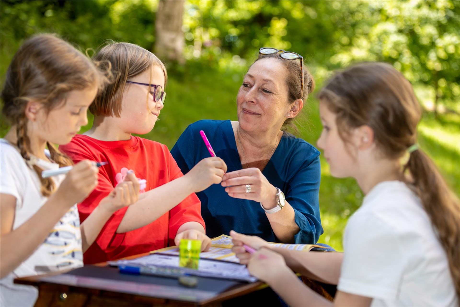 Draußen an einem Tisch ist eine Erzieherin mit drei Kindern.